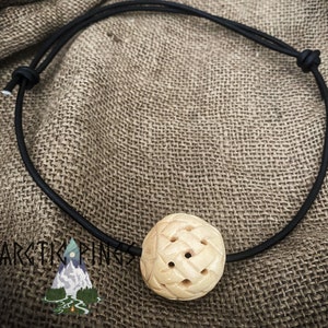 May include: A carved wooden ball pendant on a black leather cord. The ball has a geometric pattern and several small holes.
