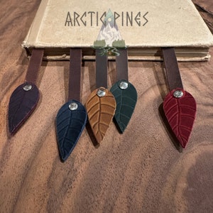 Può includere: Cinque segnalibri in pelle a forma di foglie in diversi colori: bordeaux, blu scuro, marrone, verde e viola scuro. Ogni segnalibro ha un accento in metallo argentato.