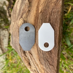 Op de afbeelding: Twee metalen sleutelhangers, een is zilver en de andere is wit. Beide hebben een gat in het midden.