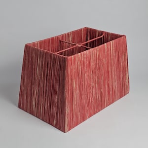 May include: A rectangular lampshade with a red and cream woven texture. The lampshade has a trapezoidal shape, wider at the base and narrower at the top. A metal frame is visible inside the shade.
