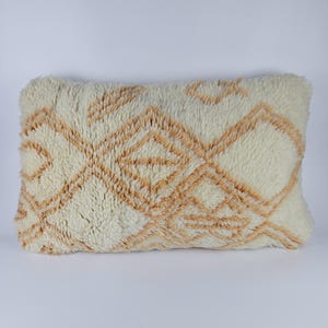 May include: A rectangular cushion with a geometric pattern in white and beige. The cushion is made from a soft, fluffy material.