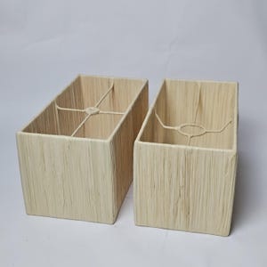 May include: Two rectangular lampshades in a natural, textured style. The shades are a light beige colour and have a woven, vertical pattern. Each shade has a metal frame inside.