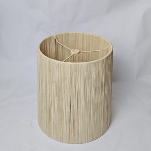 May include: Cylindrical lampshade with a light beige woven texture. The shade has an open top and bottom, with a metal frame inside. The lampshade is designed to diffuse light and add a warm, natural touch to any room. The height is approximately 25 cm.