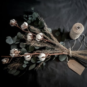 May include: A bouquet of dried eucalyptus and cotton stems with a brown paper tag that says "Coutura".