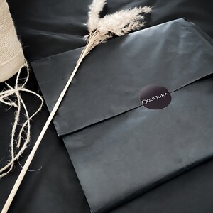 May include: A black paper gift bag with a round black sticker that says "COULTURA" in white text.