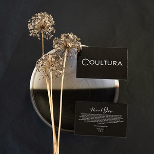 May include: Black and white thank you card with the text "Thank You" and the company name "COULTURA" printed on it. The card is sitting on a black and white ceramic bowl with dried flowers in the background.
