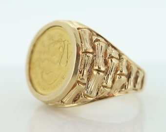 May include: A gold ring with a round coin-shaped setting featuring a detailed design. The band of the ring is textured with a bamboo pattern.