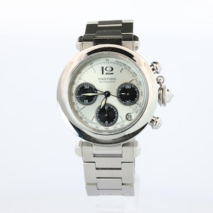 May include: A silver-tone Cartier automatic chronograph watch with a round case and a white dial. The dial features three black sub-dials, a date window at the four o'clock position, and the text Cartier Automatic. It has a metal link bracelet.