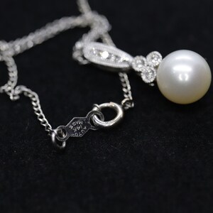 May include: A silver necklace with a pearl pendant and small diamonds. The pendant has a delicate design and the pearl is white and lustrous. The necklace has a clasp that says "AUTO K14K MADE".