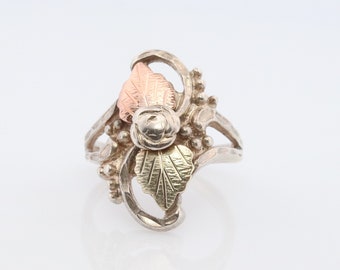 Puede incluir: Un anillo de plata con un diseño de rosa y hojas. Las hojas son verdes y doradas, y la rosa es rosa.