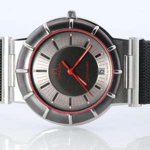 May include: A silver-toned Omega Seamaster watch with a black face and red hands. The watch has a black band with red stitching. The watch face has a date display at the 3 o'clock position.
