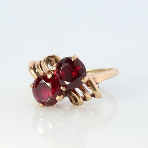 May include: A gold ring with two red gemstones set in a swirling design.