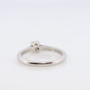 May include: A silver ring with a single diamond set in a prong setting. The ring is engraved with the words 'Cartier' and '47 017944 Pt 950  ©'.