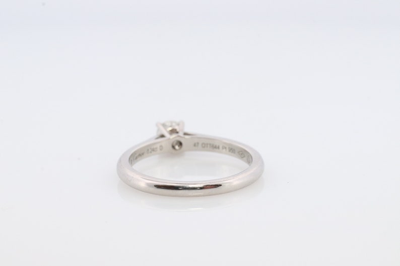 May include: A silver ring with a single diamond set in a prong setting. The ring is engraved with the words 'Cartier' and '47 017944 Pt 950  ©'.