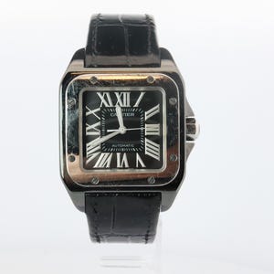 May include: A square-cased wristwatch with a silver-tone metal bezel, a black dial featuring white Roman numeral hour markers, and the text Cartier and Automatic. The watch includes a black leather strap with a textured, embossed finish.
