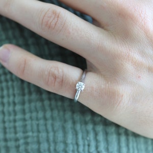 May include: A silver solitaire engagement ring with a round diamond