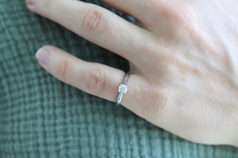 May include: A silver solitaire engagement ring with a round diamond
