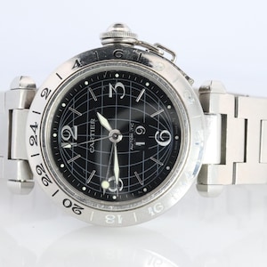 May include: A silver-toned Cartier wristwatch with a black dial and a grid pattern. The watch features white numerals and hands, and a silver bracelet. The watch face includes the word "Cartier" and "Automatic".