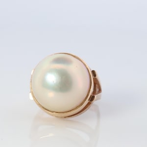 May include: A gold ring with a large, white pearl set in the center. The pearl has a slight iridescent sheen.