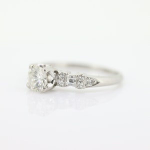 May include: A silver engagement ring with a round center diamond and smaller diamonds set in a pave setting along the band.