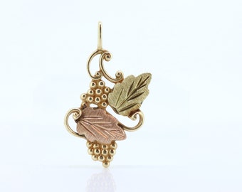 May include: A gold pendant featuring a cluster of grapes and leaves. The leaves are made of 14k gold and have a textured finish. The pendant is a beautiful and delicate piece of jewelry.