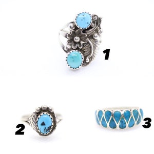 May include: Three turquoise rings with silver settings. The first ring has a floral design with two turquoise stones. The second ring has a single turquoise stone with a feather design. The third ring has a band of turquoise stones in a geometric pattern.
