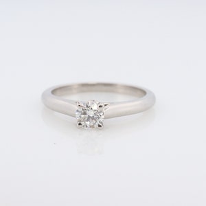 May include: A silver solitaire engagement ring with a round, clear diamond in the center.