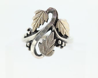 May include: A silver ring featuring three gold leaves and a vine design.