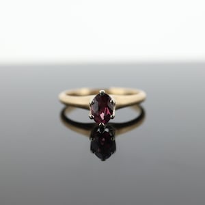 Op de afbeelding: Een gouden ring met een enkele, ovale, donkerpaarse edelsteen.