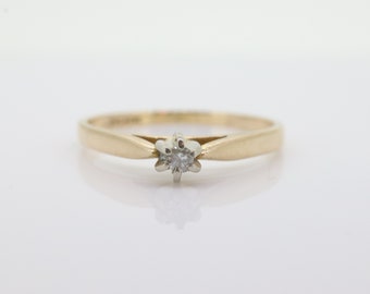 May include: A simple gold band ring with a single, small, round diamond in the center.
