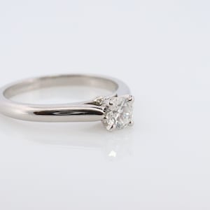 May include: A silver solitaire engagement ring with a round diamond set in a simple band.