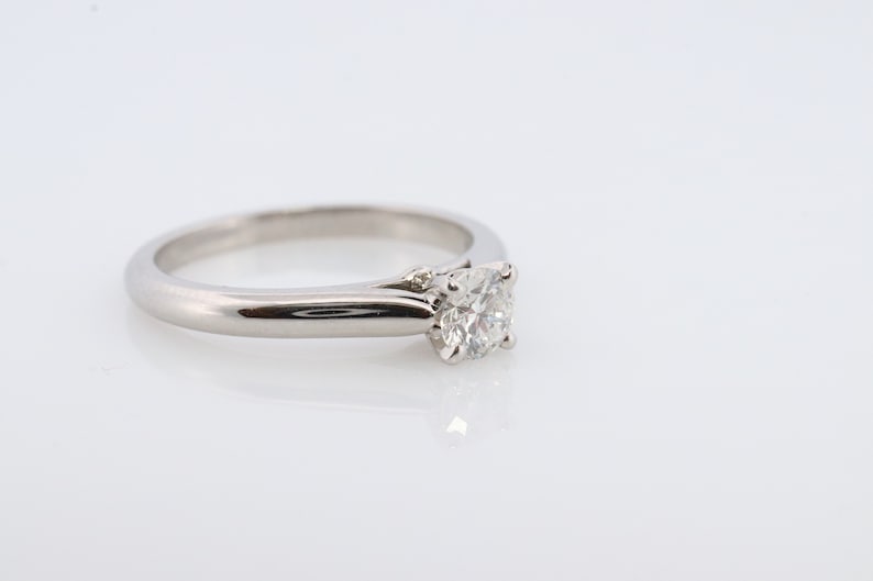 May include: A silver solitaire engagement ring with a round diamond set in a simple band.