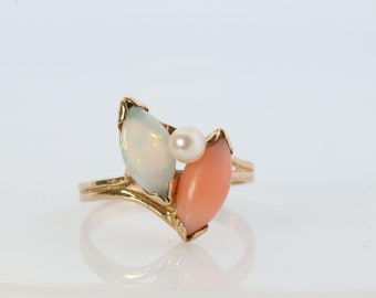 Può includere: Un anello d'oro con un opale bianco, una perla e una pietra di corallo rosa.