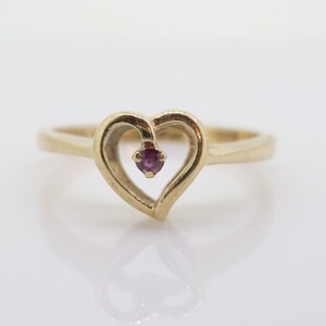 Può includere: Un anello d'oro a forma di cuore con una piccola pietra preziosa viola al centro.