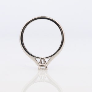 May include: A silver solitaire engagement ring with a single round diamond in a prong setting. The ring has a thin band and a simple design.