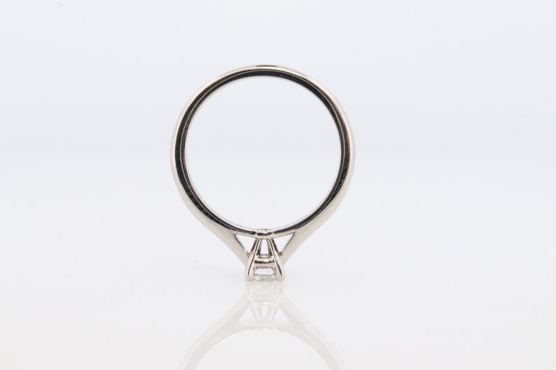 May include: A silver solitaire engagement ring with a single round diamond in a prong setting. The ring has a thin band and a simple design.