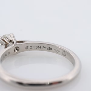 May include: A platinum engagement ring with a single round diamond set in a four-prong setting. The band is plain and the inside of the band is inscribed with '47 OTT644 Pt 950'.