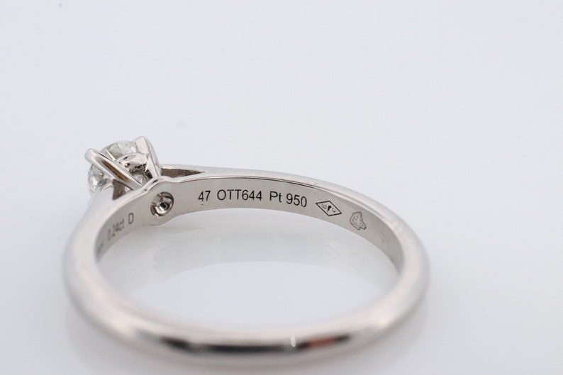 May include: A platinum engagement ring with a single round diamond set in a four-prong setting. The band is plain and the inside of the band is inscribed with '47 OTT644 Pt 950'.