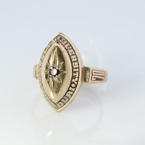 May include: A gold-toned ring with a red stone set in a star design. The ring is engraved with the words "DUQUESNE UNIVERSITY".