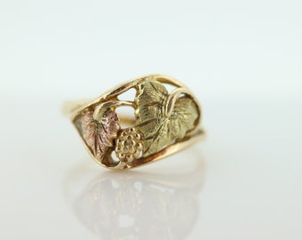 May include: A gold ring with a delicate design featuring three leaves and a cluster of berries. The leaves are crafted in green, pink, and yellow gold.