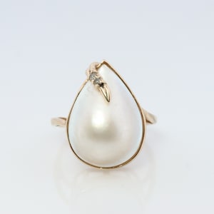 May include: A gold ring with a large pearlescent white teardrop-shaped stone and two small diamonds set in the gold band.