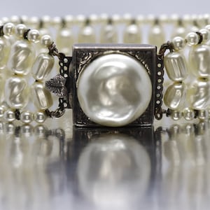 May include: A white pearl bracelet with a silver clasp featuring a large pearl in the center.