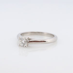 May include: A silver solitaire engagement ring with a single round diamond set in a prong setting.