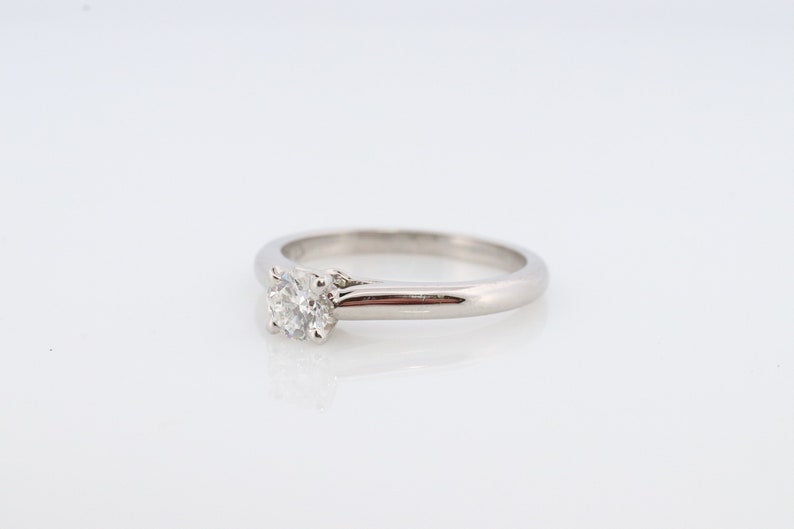May include: A silver solitaire engagement ring with a single round diamond set in a prong setting.