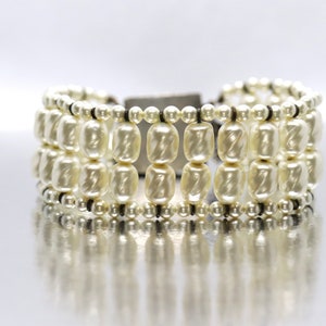 May include: A white pearl bracelet with multiple rows of pearls and a black cord closure.