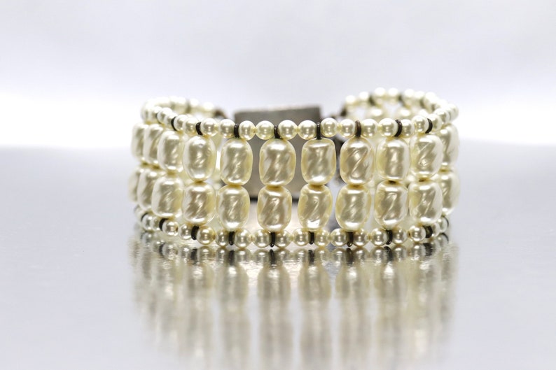 May include: A white pearl bracelet with multiple rows of pearls and a black cord closure.