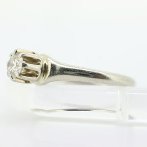 May include: A silver engagement ring with a single round diamond set in a prong setting. The band is simple and elegant.