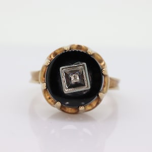 May include: A gold ring with a black onyx stone set in a square shape. A small diamond is set in the center of the onyx stone.