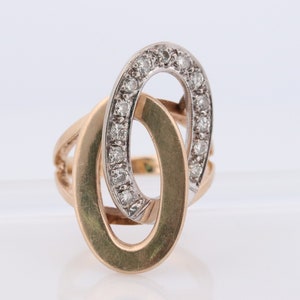 May include: A gold and white ring with a diamond-encrusted oval design. The ring is made of two interlocking ovals, one of which is set with diamonds.