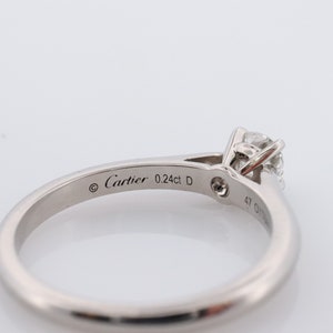 May include: A silver Cartier ring with a single round diamond. The ring is engraved with the words 'Cartier 0.24ct D'.